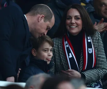 A family at a sports event, a man whispers to a boy while a woman smiles, all wearing winter clothes and scarves.