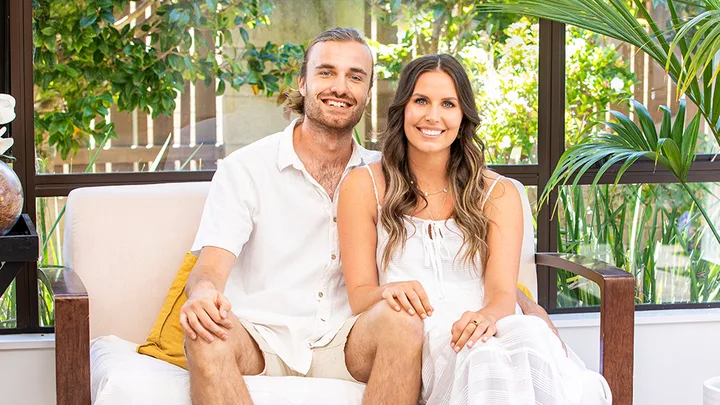 Man and woman smiling and sitting on a bench indoors, surrounded by greenery and natural light.