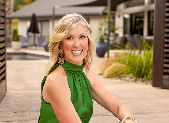 Unknown woman smiling outdoors, wearing a green dress and statement earrings with a blurred background.