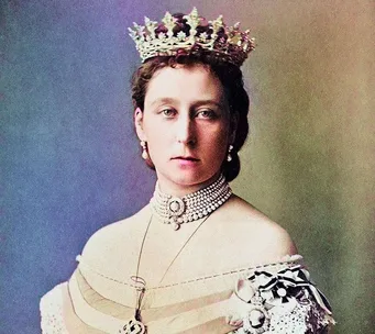 A woman wearing a jeweled tiara and pearl jewelry, dressed in a period outfit with ornate decorations.
