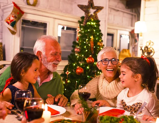 Family celebrating Christmas dinner with two children, an older man, and a woman by a decorated tree.