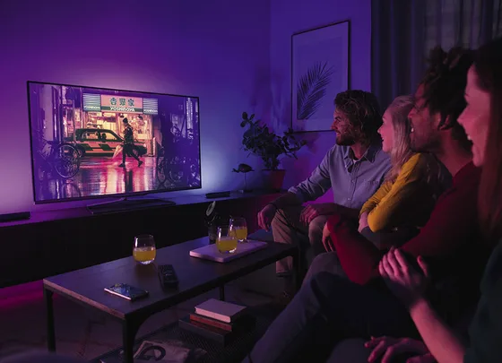 Group of four people watching TV in a dimly lit room with drinks on the table.