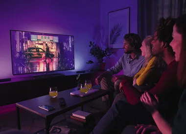 Group of four people watching TV in a dimly lit room with drinks on the table.