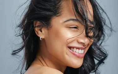 Smiling woman with windswept hair and silver hoop earrings.