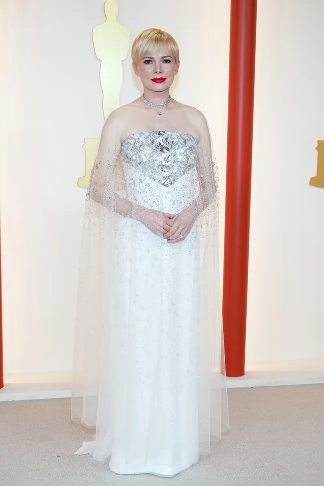 A person in a white, sparkling gown at an event, standing in front of an Oscar silhouette.