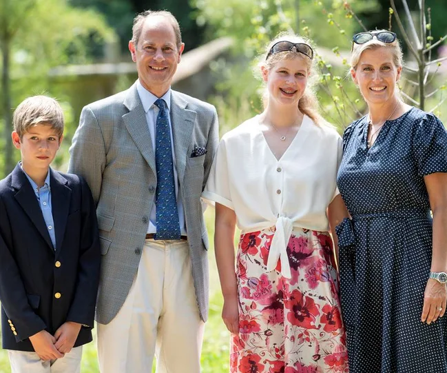 Family of four smiling outdoors, including two adults and two children dressed in summer attire.