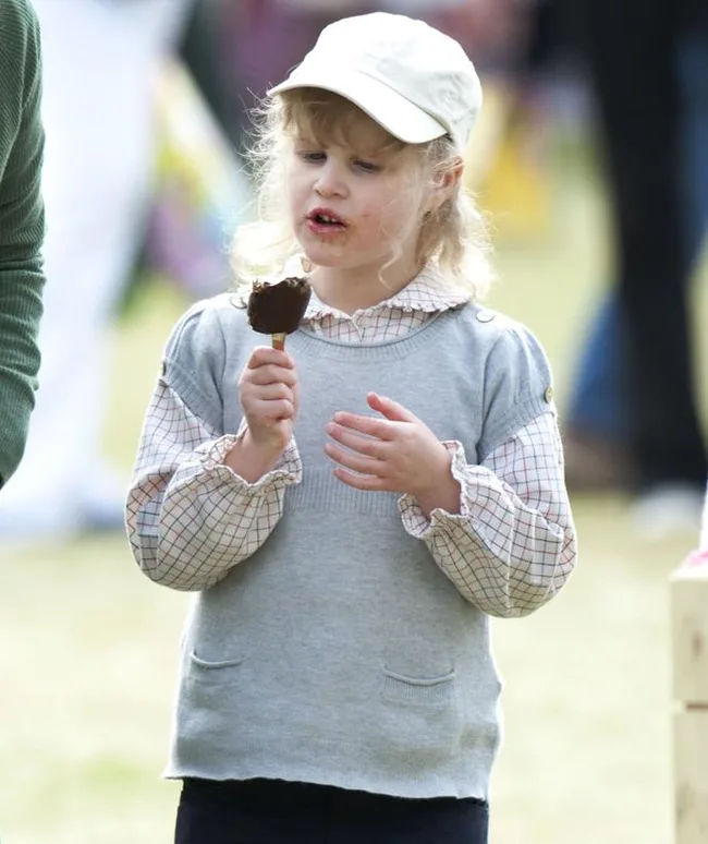 A child in a cap eating a chocolate ice cream outdoors.