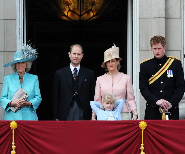 Royal family members stand on a balcony, with a young child in front during a formal event.