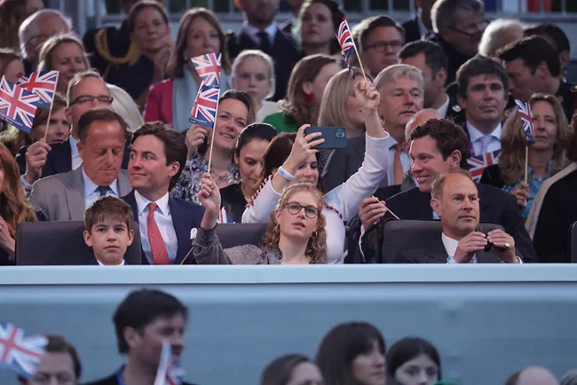 A crowd of people at an event, some holding British flags and taking photos, appear to be enjoying the moment.