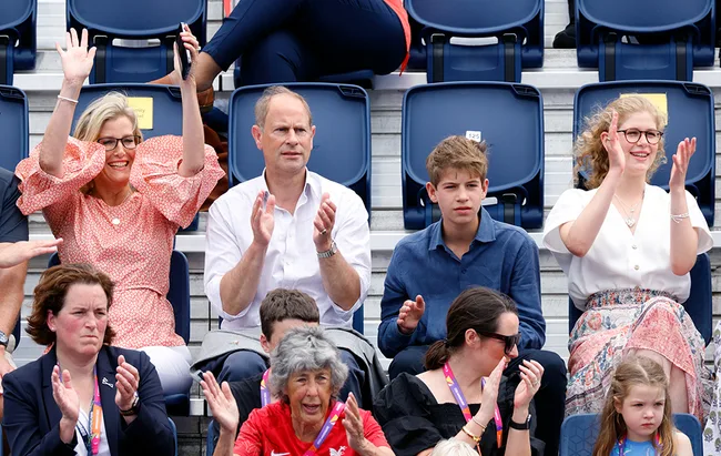 Audience cheering and clapping in a stadium, seated in rows, with a mix of ages and expressions of excitement.