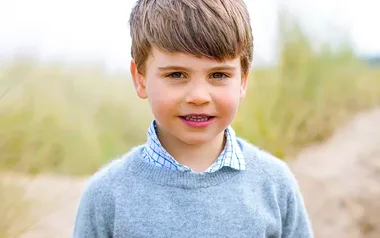 A young child with brown hair in a gray sweater outdoors, smiling at the camera.