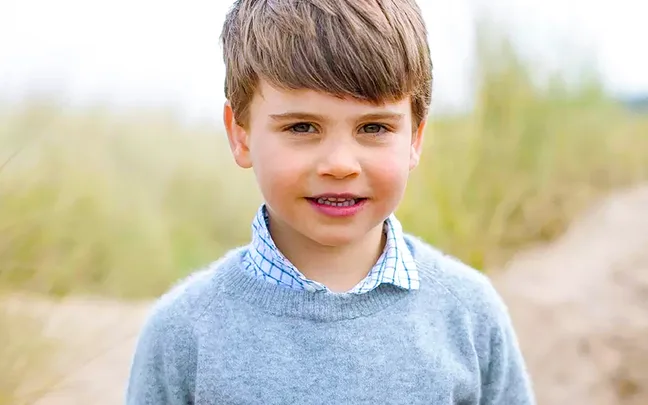 A young child with brown hair in a gray sweater outdoors, smiling at the camera.