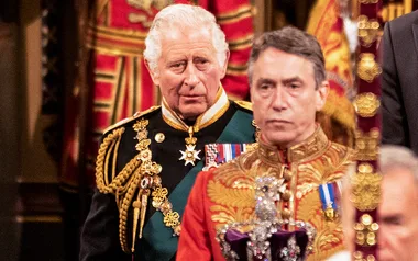 Two men in ornate ceremonial uniforms, with gold embellishments, at a formal event indoors.