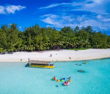 Aerial view of a tropical beach with a yellow boat and people swimming in clear blue water near palm trees.