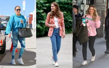 Three women wearing casual outfits walking outdoors; one in blue, one in pink blazer, and one in pink sweater holding coffee.
