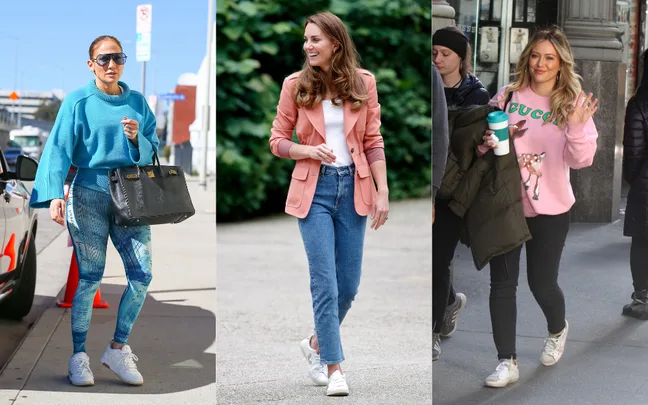 Three women wearing casual outfits walking outdoors; one in blue, one in pink blazer, and one in pink sweater holding coffee.