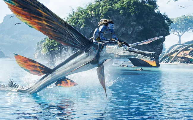 A Na'vi character from "Avatar" riding a flying creature over a serene body of water.
