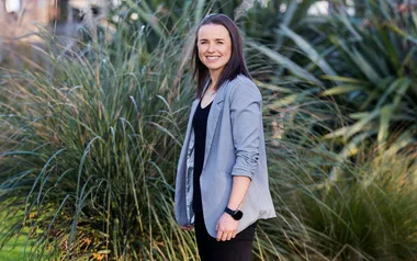 Bernadine Bezuidenhout in a grey blazer standing in front of some green plants