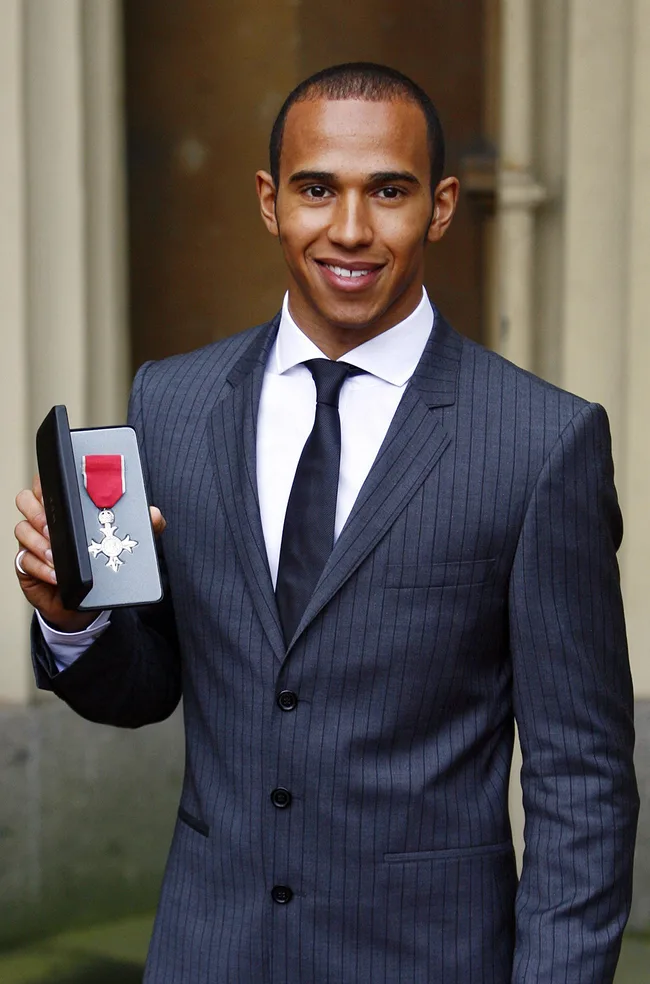 Man in a suit smiling and holding a box with a medal.