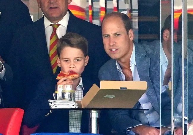 A young boy eats pizza while sitting next to a man in a suit, both looking intently.