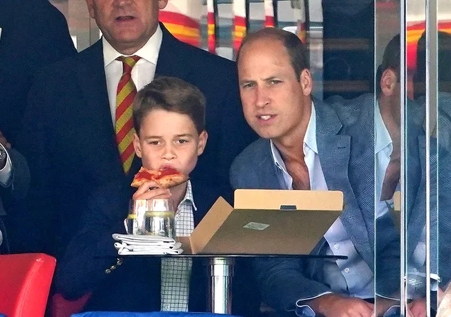 A young boy eats pizza while sitting next to a man in a suit, both looking intently.