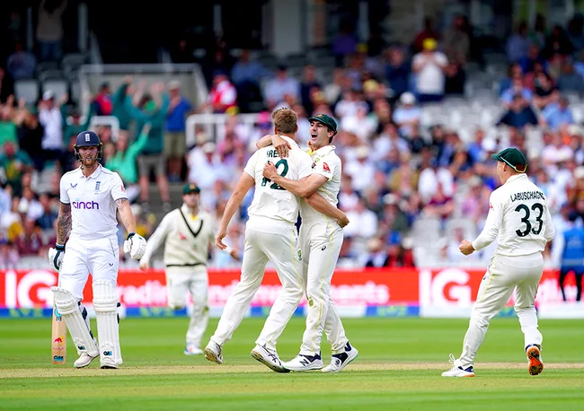 Cricketers celebrate a wicket against England; one batsman stands nearby with crowd in background.