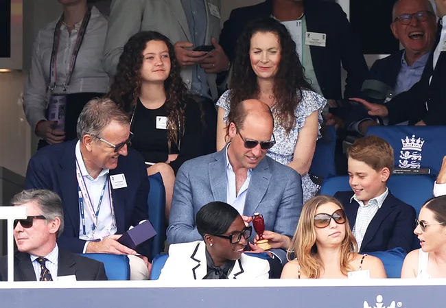 Group of people seated in a sports stadium, engaging and smiling, some wearing sunglasses.