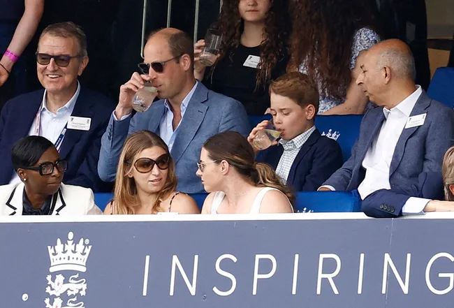 A group of people sitting in a stadium box, some wearing sunglasses, with a sign saying "Inspiring" visible.