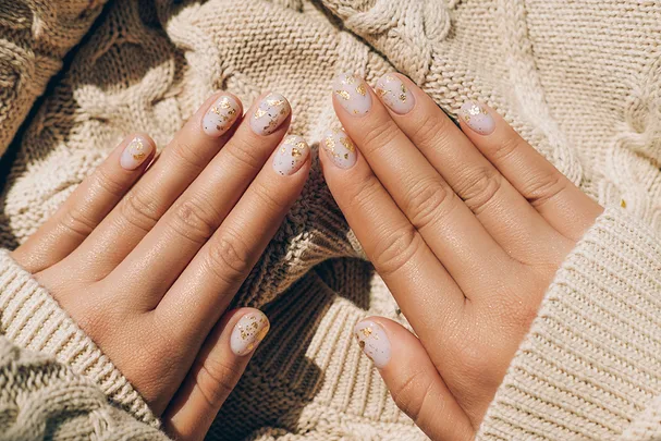 Hands with pastel nails and gold flakes on a cream knitted sweater background.