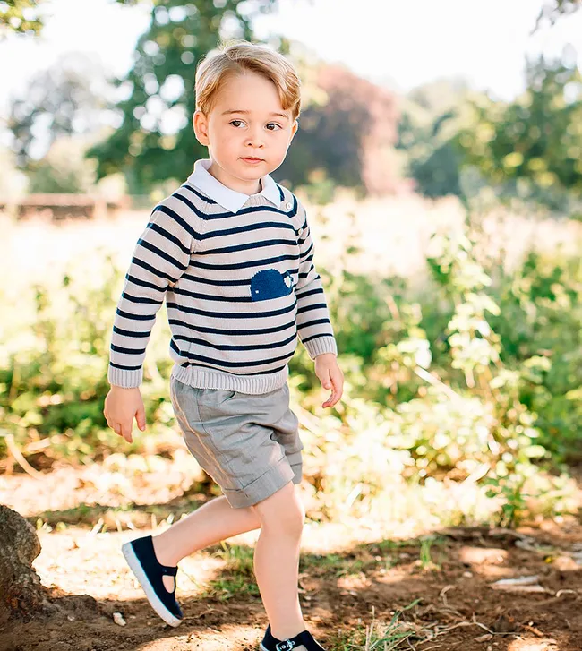 Toddler in striped sweater and shorts walking outdoors on a sunny day.