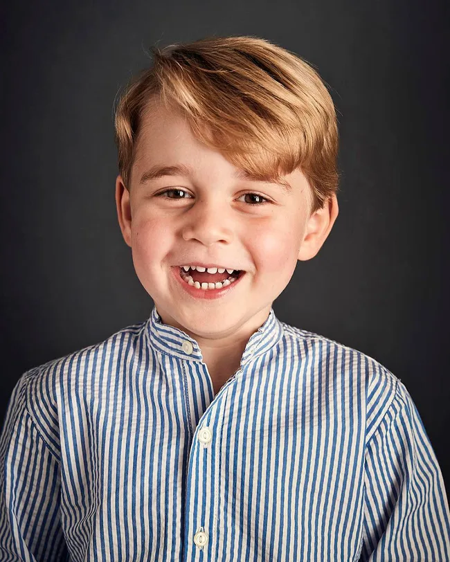 A young boy with light brown hair smiling, wearing a blue and white striped shirt against a plain background.