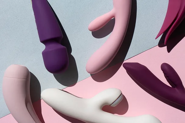 Various vibrators in shades of purple, pink, and white are arranged on a light blue and pink background.