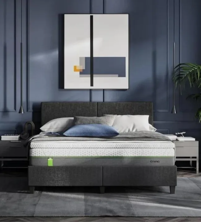 A modern bedroom with a gray upholstered bed, minimalist art, and dark blue walls.
