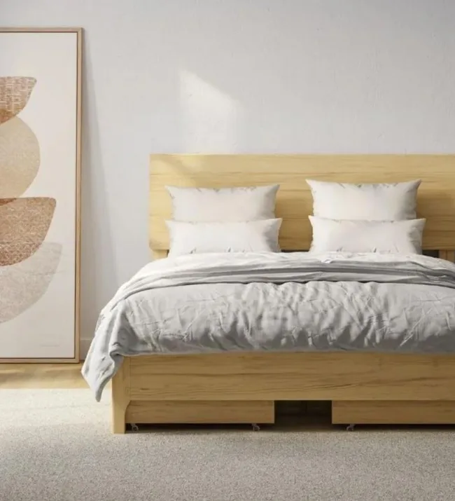A neatly made bed with light grey bedding and wooden headboard, beside a large abstract art piece on the wall.