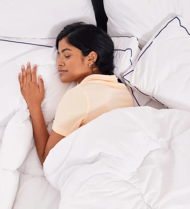 Person sleeping peacefully in a bed with white sheets and pillows.