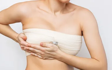 A person wearing a beige compression bandage around the chest, adjusting it with hands, against a plain background.