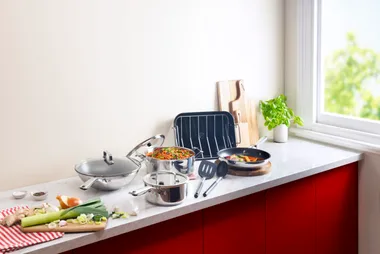 Kitchen counter with stainless steel cookware, fresh vegetables, and utensils near a sunny window.