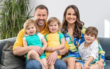 Family of five sitting on a sofa, smiling; two adults and three young children.