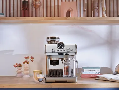 Espresso machine on kitchen countertop with books and decor items in the background.