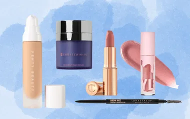 Various makeup products on a blue background, including Fenty Beauty foundation, Emma Lewisham serum, and lipsticks.