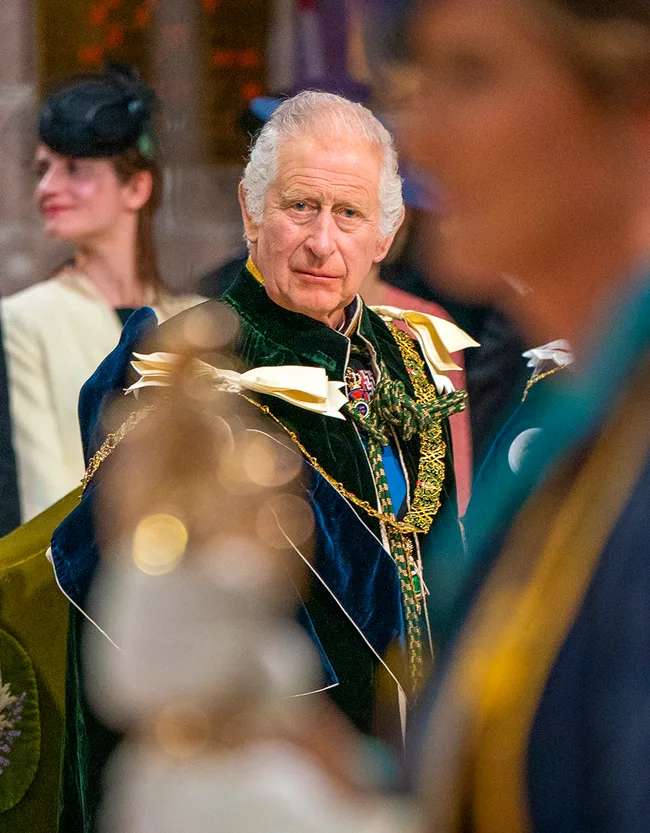 A man wearing ceremonial attire with a thoughtful expression at an event, blurred figures in the foreground.