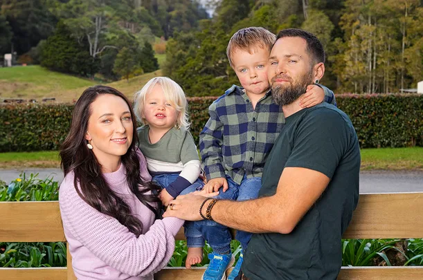 A family of four poses together outdoors, with trees and greenery in the background.
