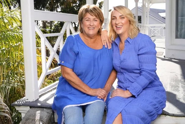 Two women in blue dresses sitting on a porch, smiling at the camera.