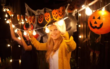 Woman decorating for Halloween with pumpkin lanterns and lights, smiling in a festive setting.