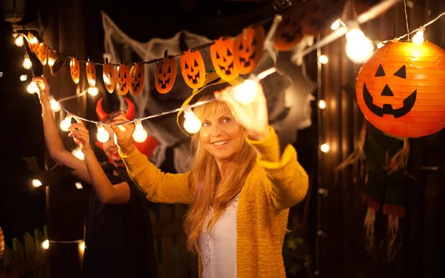 Woman decorating for Halloween with pumpkin lanterns and lights, smiling in a festive setting.