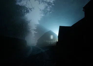 Misty night road with silhouette of a barn illuminated by blue light in the distance.