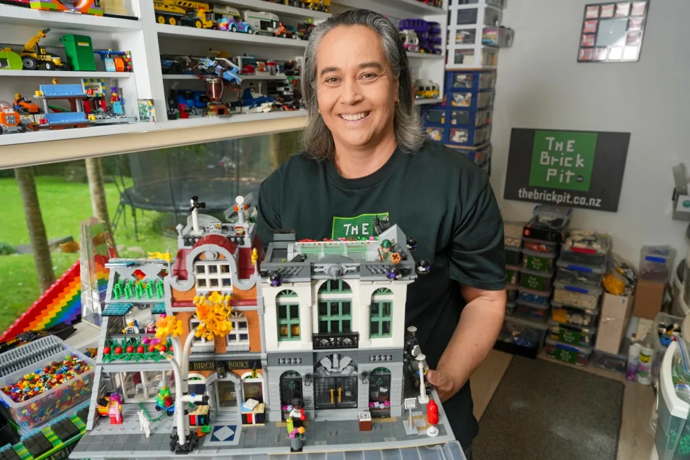 Person holding a detailed LEGO building in a room filled with LEGO sets and containers.