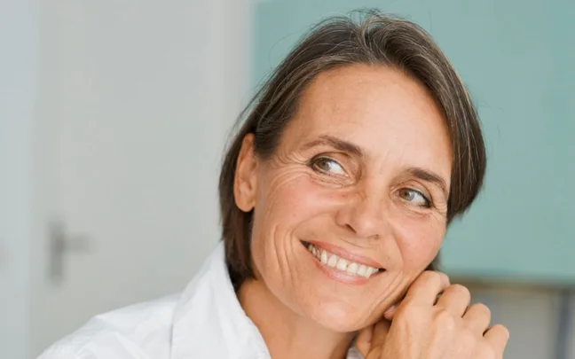 A smiling woman with short brown hair wearing a white shirt, looking off-camera.