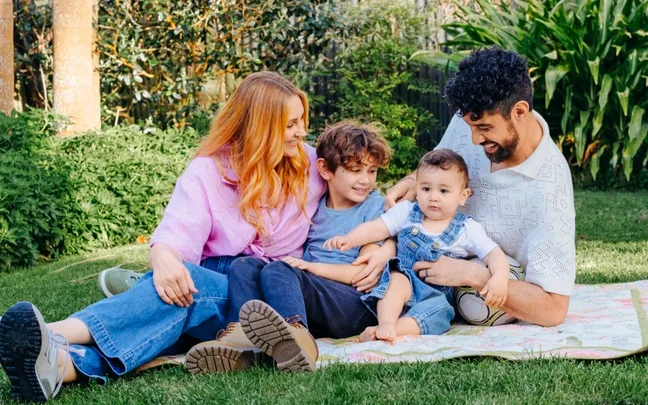 Family sitting on a blanket in a garden, smiling and interacting with their children.