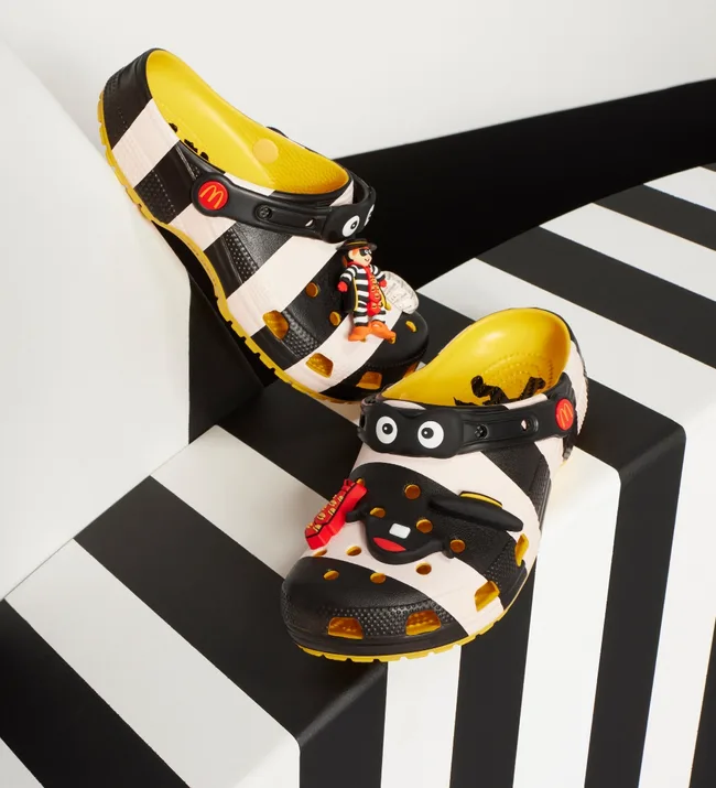 Black and white checkered Crocs with McDonald's Hamburglar charm and yellow interior on a striped surface.